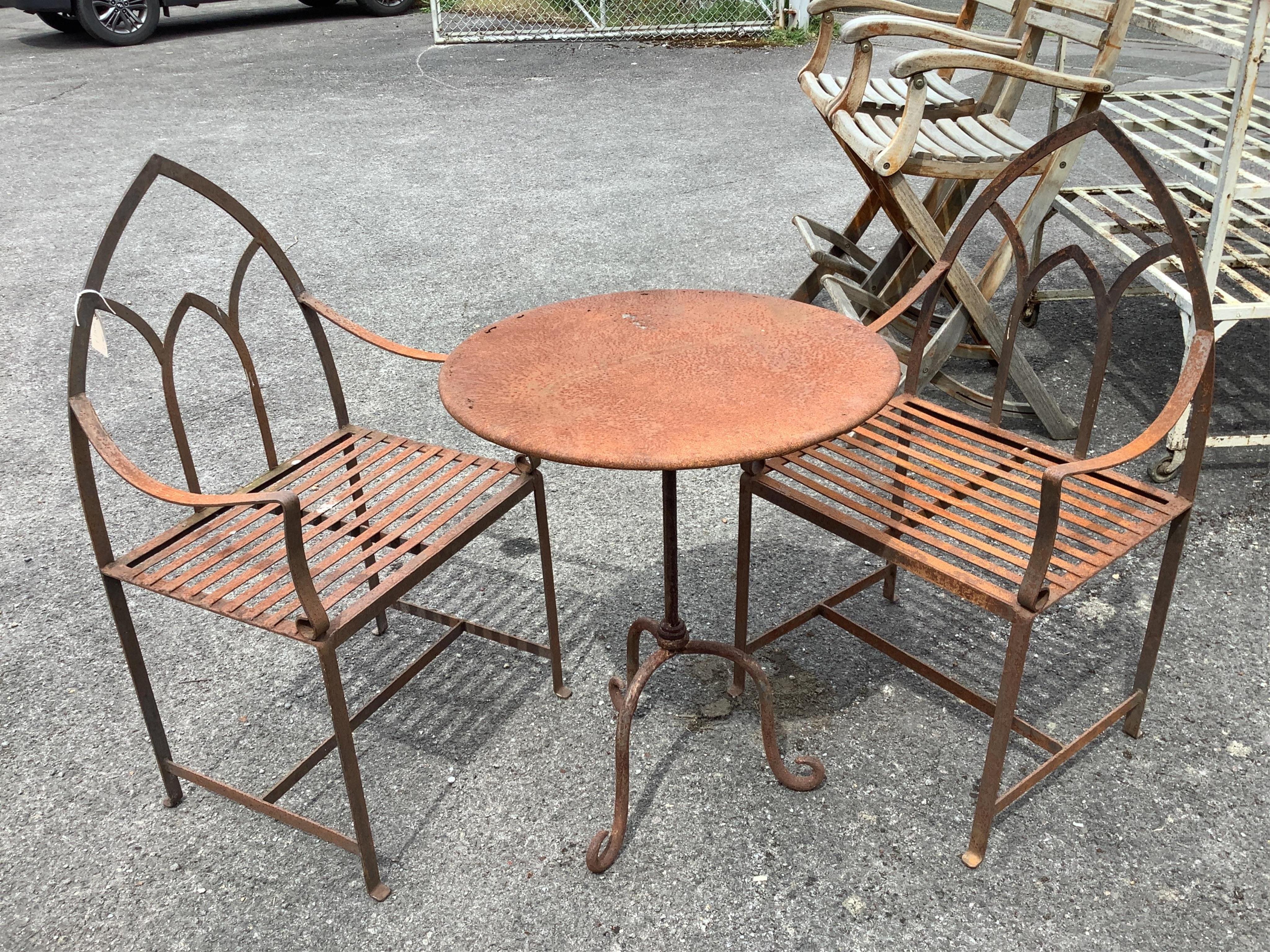 A weathered wrought iron circular garden table, diameter 60cm, height 76cm, together with a pair of wrought iron Gothic style garden chairs